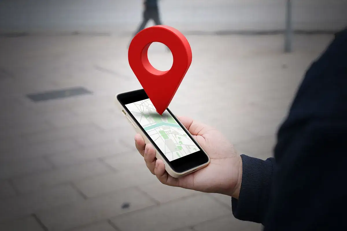 Dłoń trzyma smartfon z mapą, a nad nim unosi się czerwona pinezka. W ten sposób łatwo dowiedzieć się, jak wysłać pinezkę.