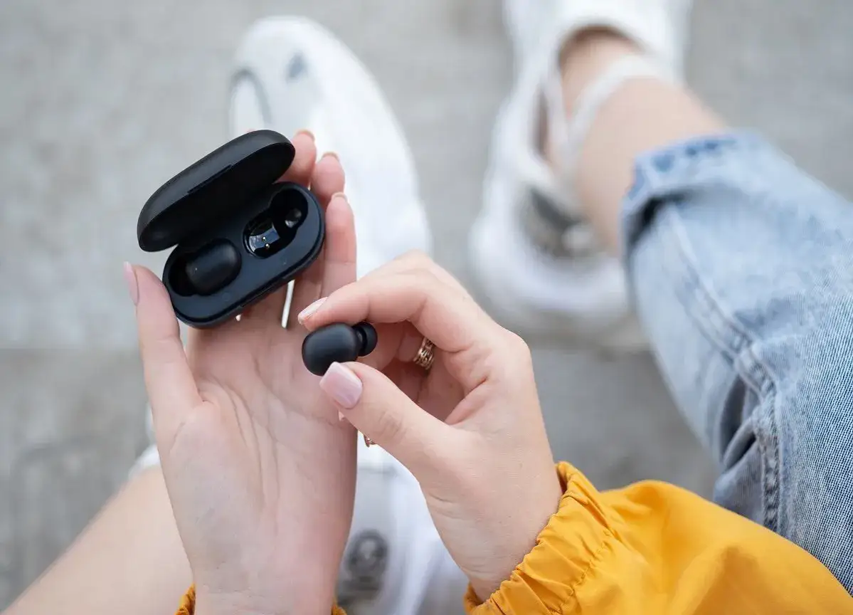 Dłonie trzymają czarne słuchawki bluetooth i etui. Dowiedz się, jak zresetować słuchawki bluetooth, gdy masz problem z połączeniem.