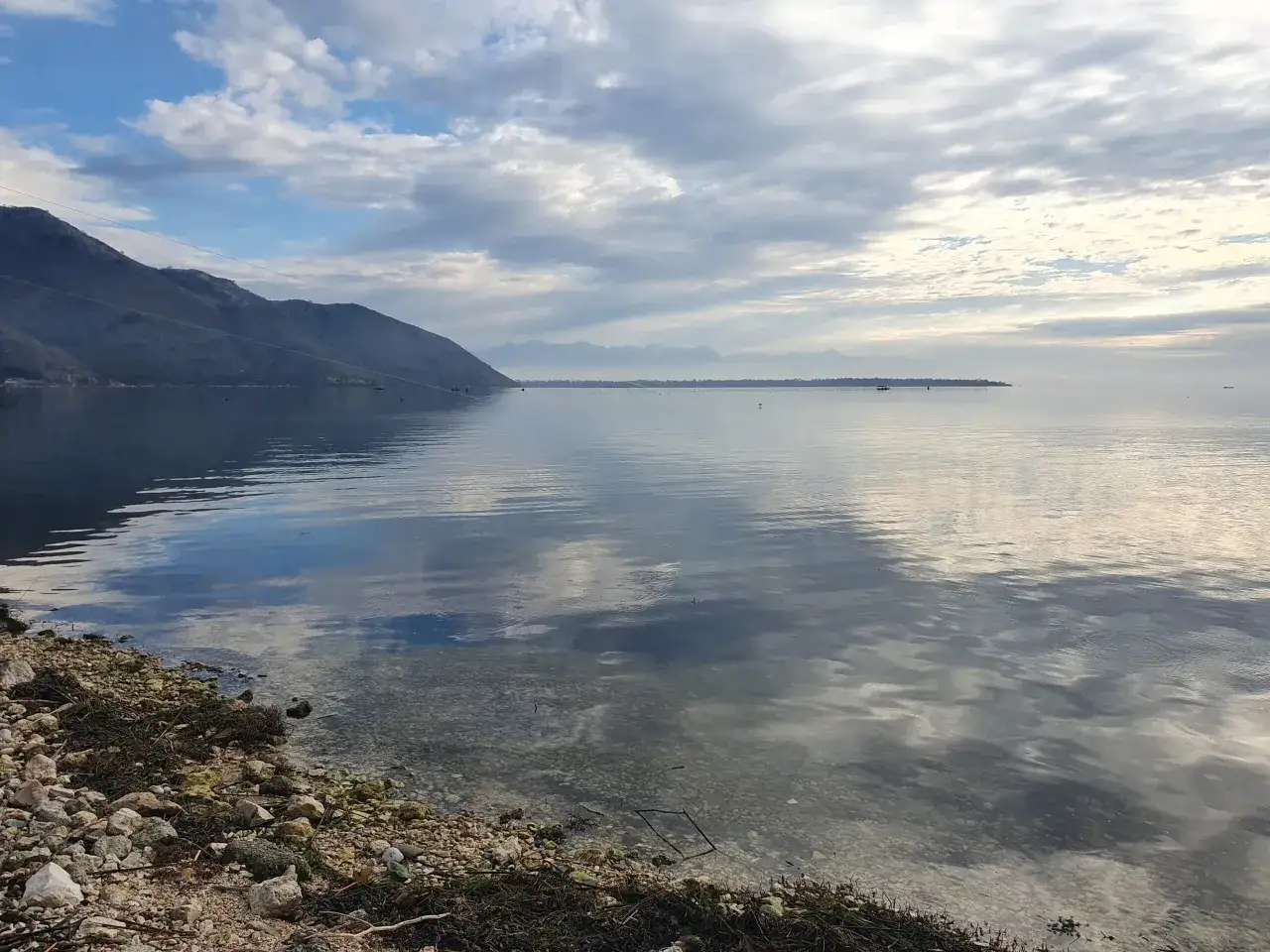 Spokojne morze w Czarnogórze we wrześniu. Góry w oddali, chmury odbijające się w wodzie.