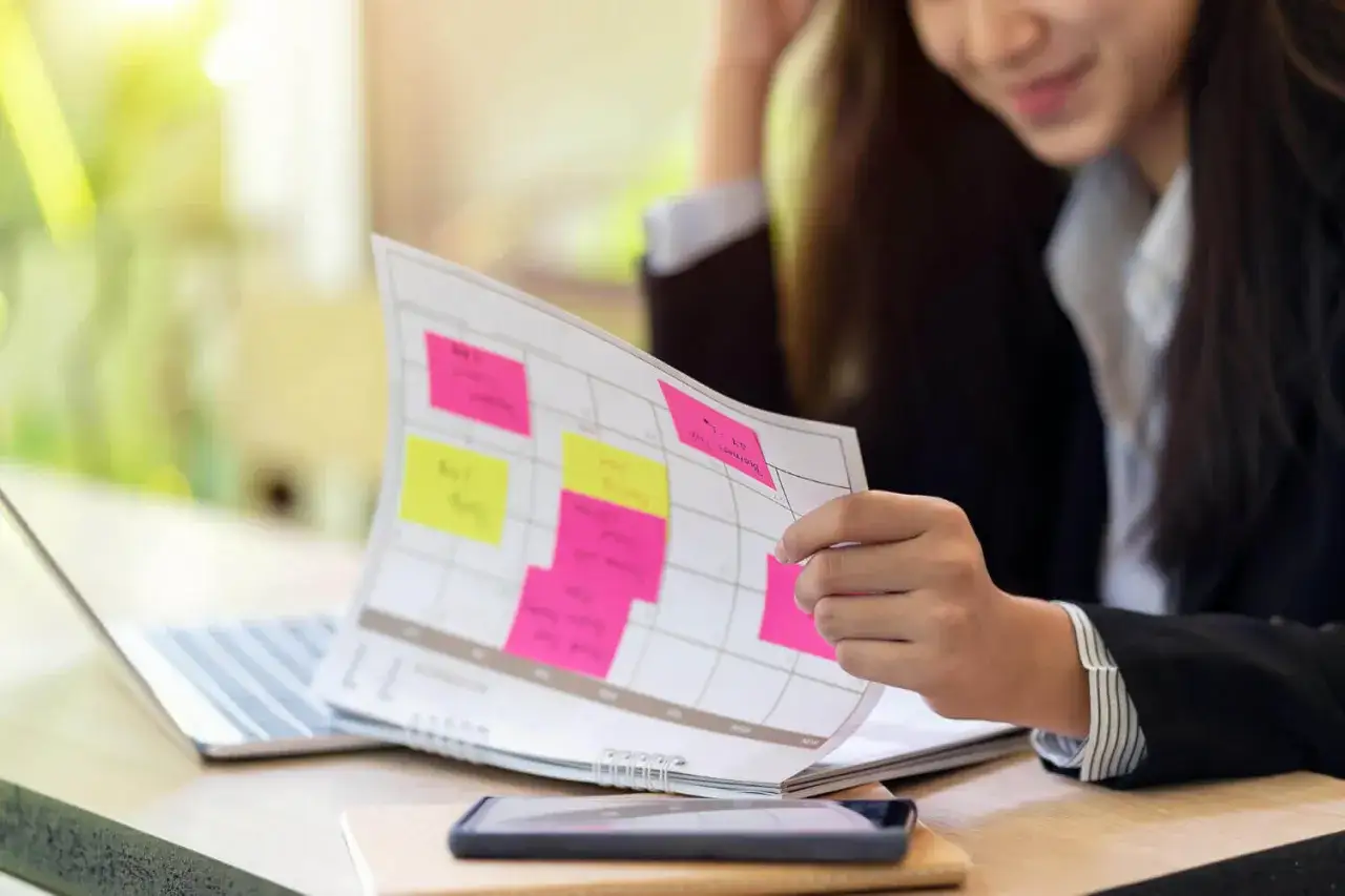 Kobieta planuje zadania na kalendarzu z kolorowymi karteczkami. To przykład metodyki pracy, która pomaga w organizacji.