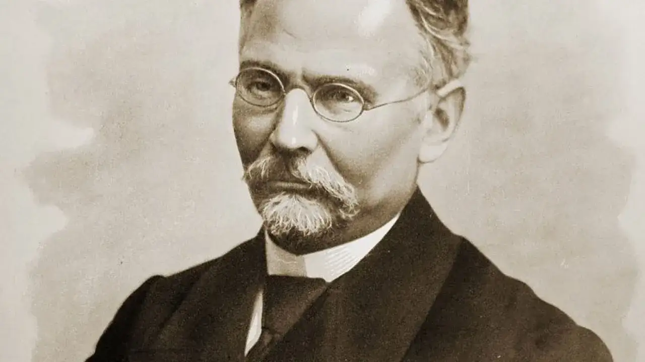 Portret mężczyzny w okularach i z wąsami, ubranego w garnitur.