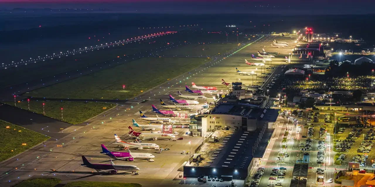 Nocne lotnisko z wieloma samolotami na płycie. Czy które lotnisko większe Kraków czy Katowice? To zdjęcie pokazuje ruchliwe lotnisko.