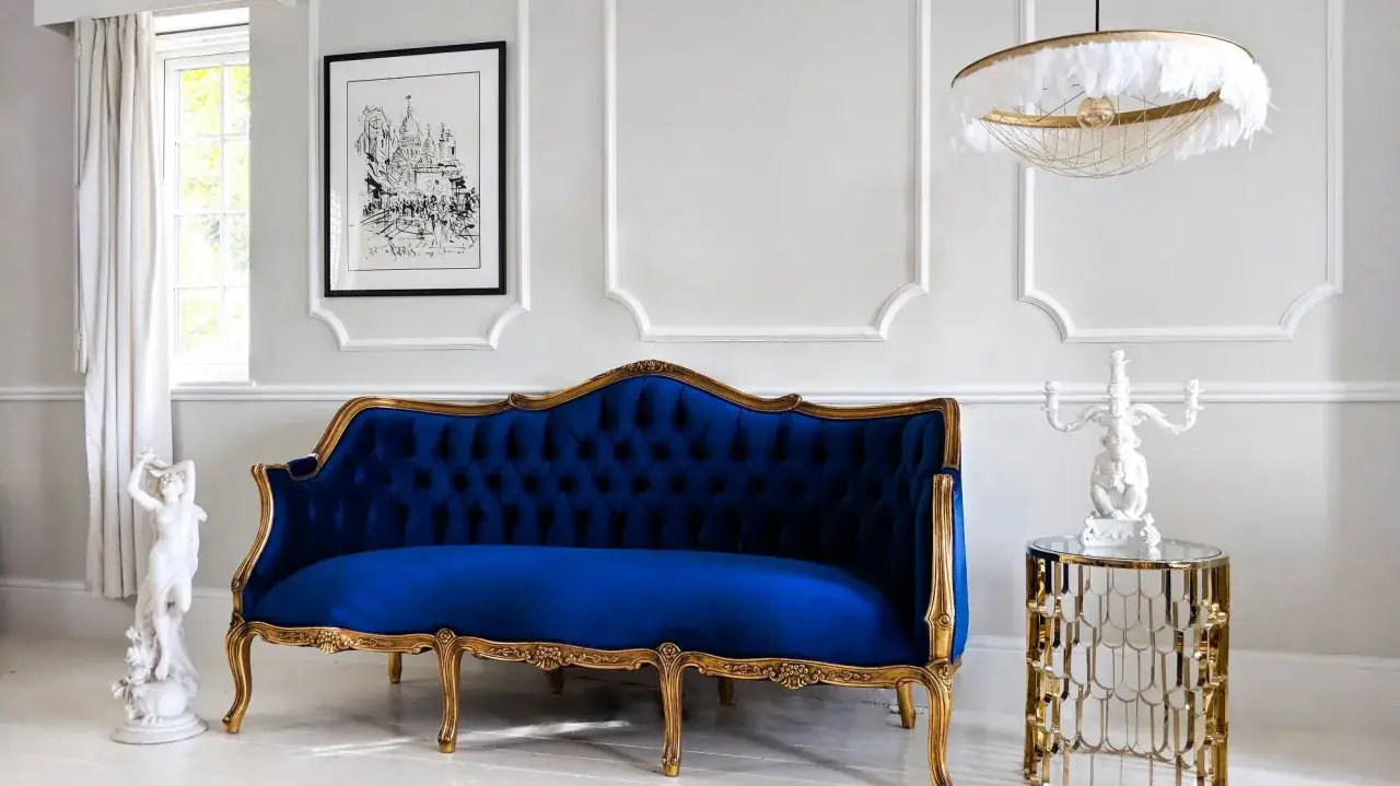 Eleganckie mieszkanie w stylu paryskim: granatowa sofa, złote zdobienia, rzeźba i obraz.