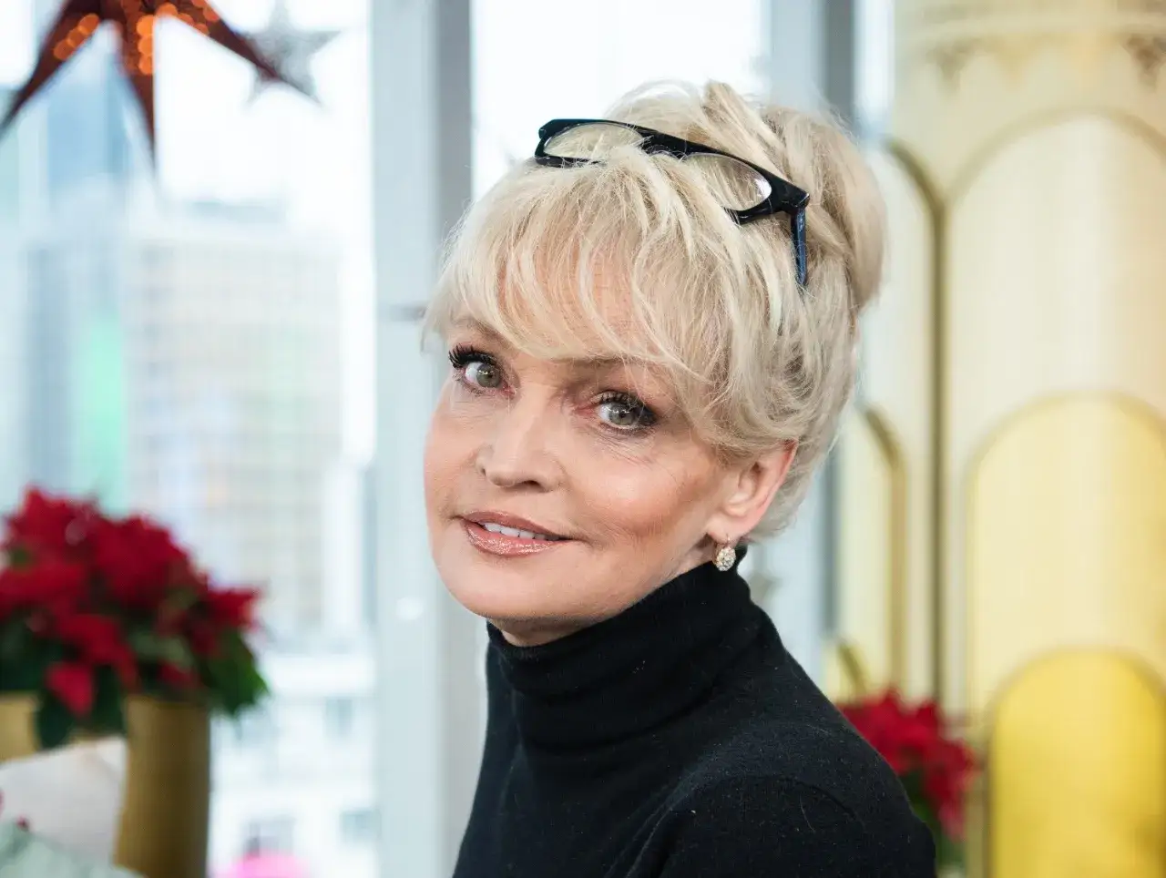 Adrianna Biedrzyńska z okularami na blond włosach, uśmiechnięta, w czarnym golfie.