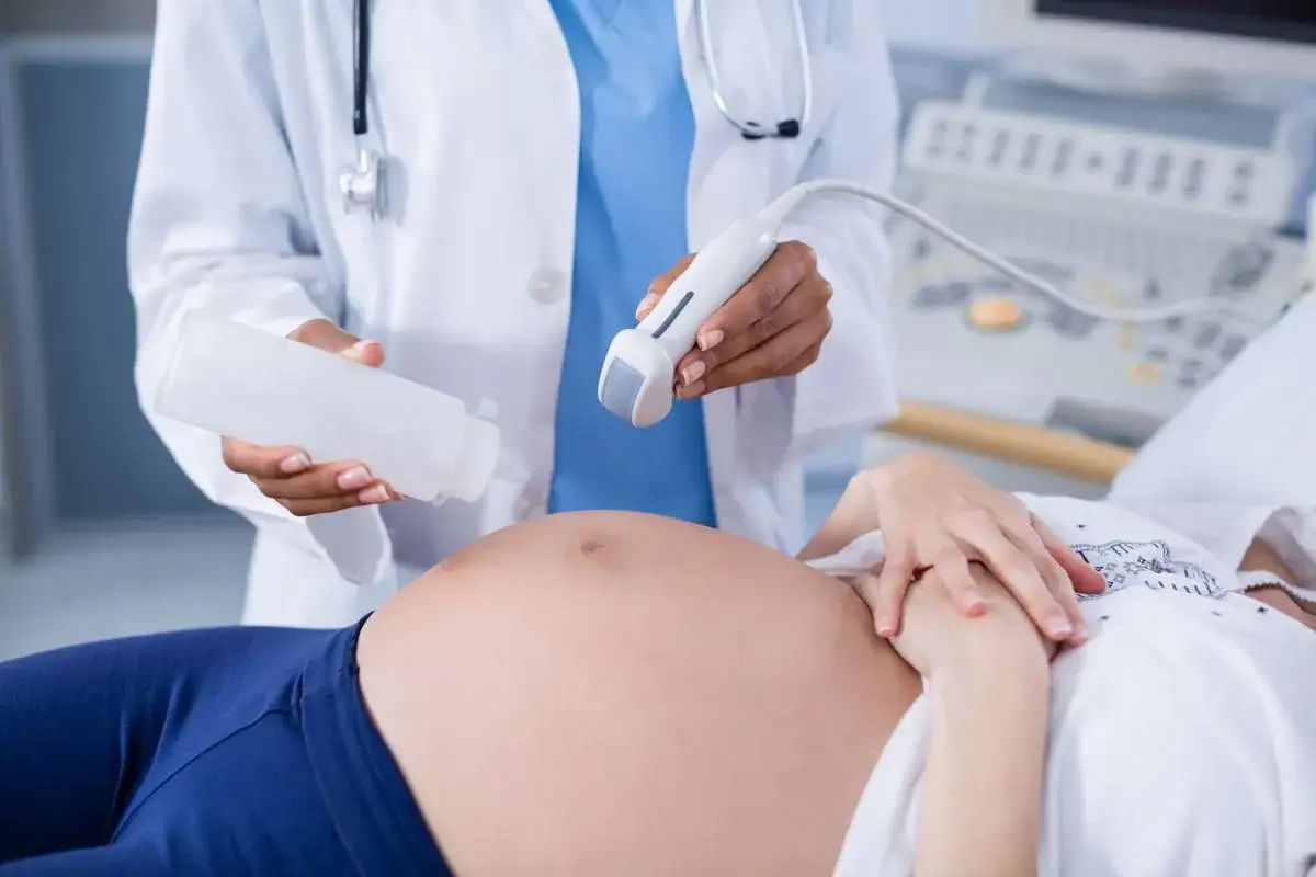 Badania prenatalne w 12 tygodniu ciąży: lekarz aplikuje żel na brzuch pacjentki przed badaniem USG.