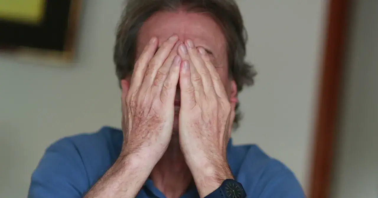 Mężczyzna zakrywa twarz dłońmi, widać zegarek na nadgarstku.