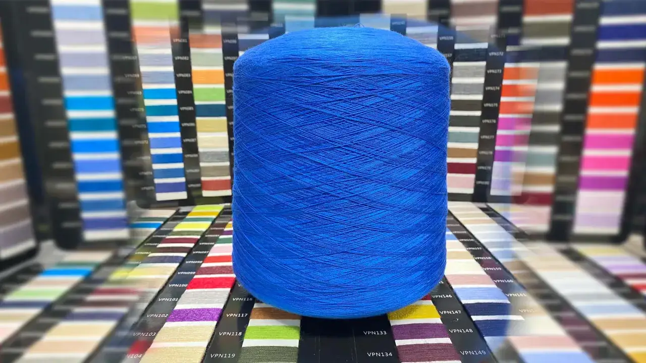 Duża, niebieska rolka włóczki, idealna do tworzenia ubrań z tencelu. W tle palety kolorów.