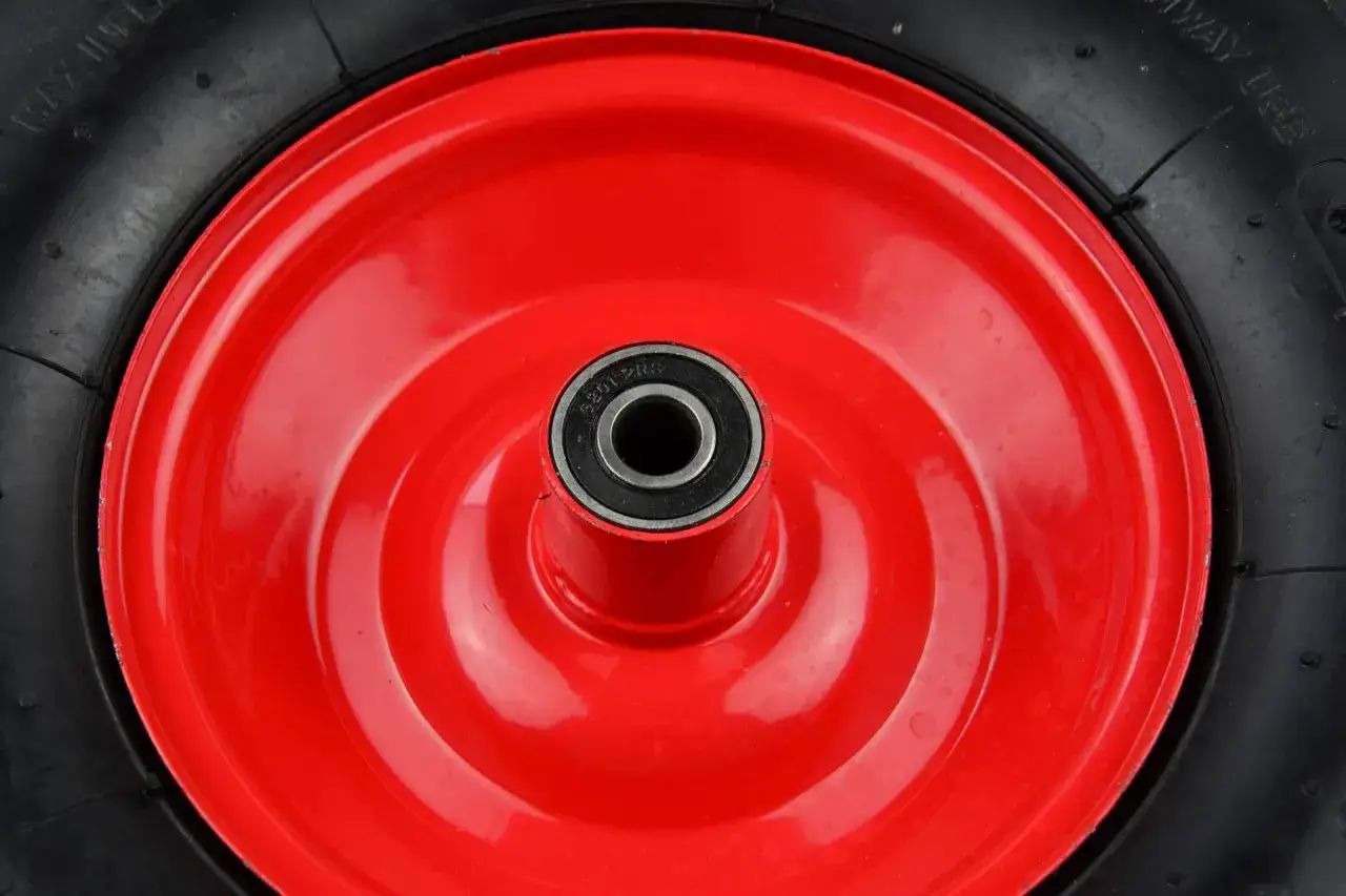 Czerwone koło taczki z czarną oponą i łożyskiem w środku.