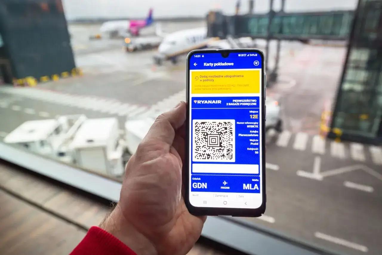 Na ekranie smartfona widać, jak wygląda bilet lotniczy Ryanair: kod QR, numer rezerwacji, miejsce 12E i trasę Gdańsk-Malta.