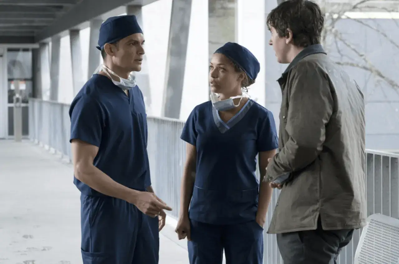 Trzech lekarzy w granatowych uniformach rozmawia na korytarzu szpitalnym. Jeden z nich, w brązowej kurtce, wydaje się być pacjentem. To scena z serialu "the good doctor".