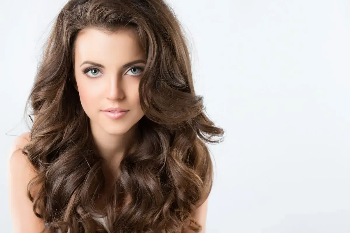 Piękna kobieta z falowanymi brązowymi włosami, idealna inspiracja do fryzury dla pociągłej twarzy. Galeria fryzur.