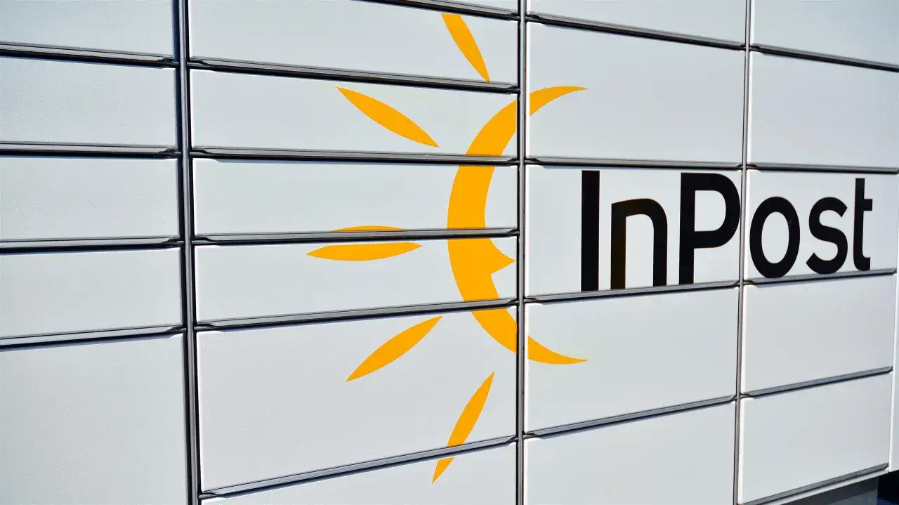 Zbliżenie na białą paczkomat InPost z żółtym logo i czarnym napisem.
