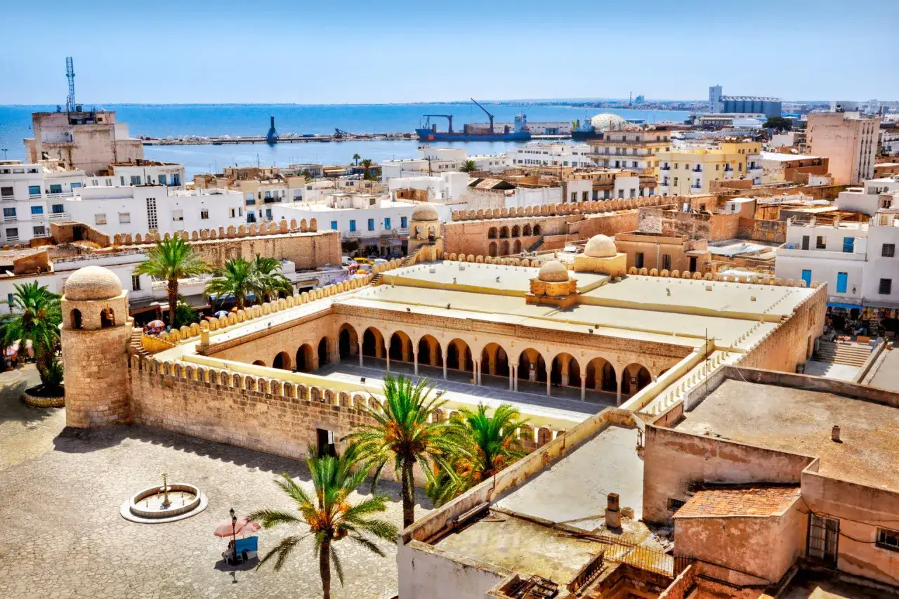 Widok z lotu ptaka na medynę Sousse z meczetem, palmami i morzem w tle.