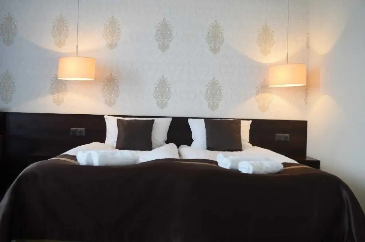 Przytulne łóżko hotelowe z dwoma lampkami. Zastanawiasz się, od ilu lat można wynająć hotel? Zazwyczaj od 18 lat.