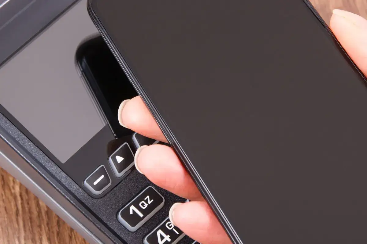 Zbliżenie na dłoń trzymającą telefon nad terminalem płatniczym. Szybki sposób, jak doladowac telefon Play.