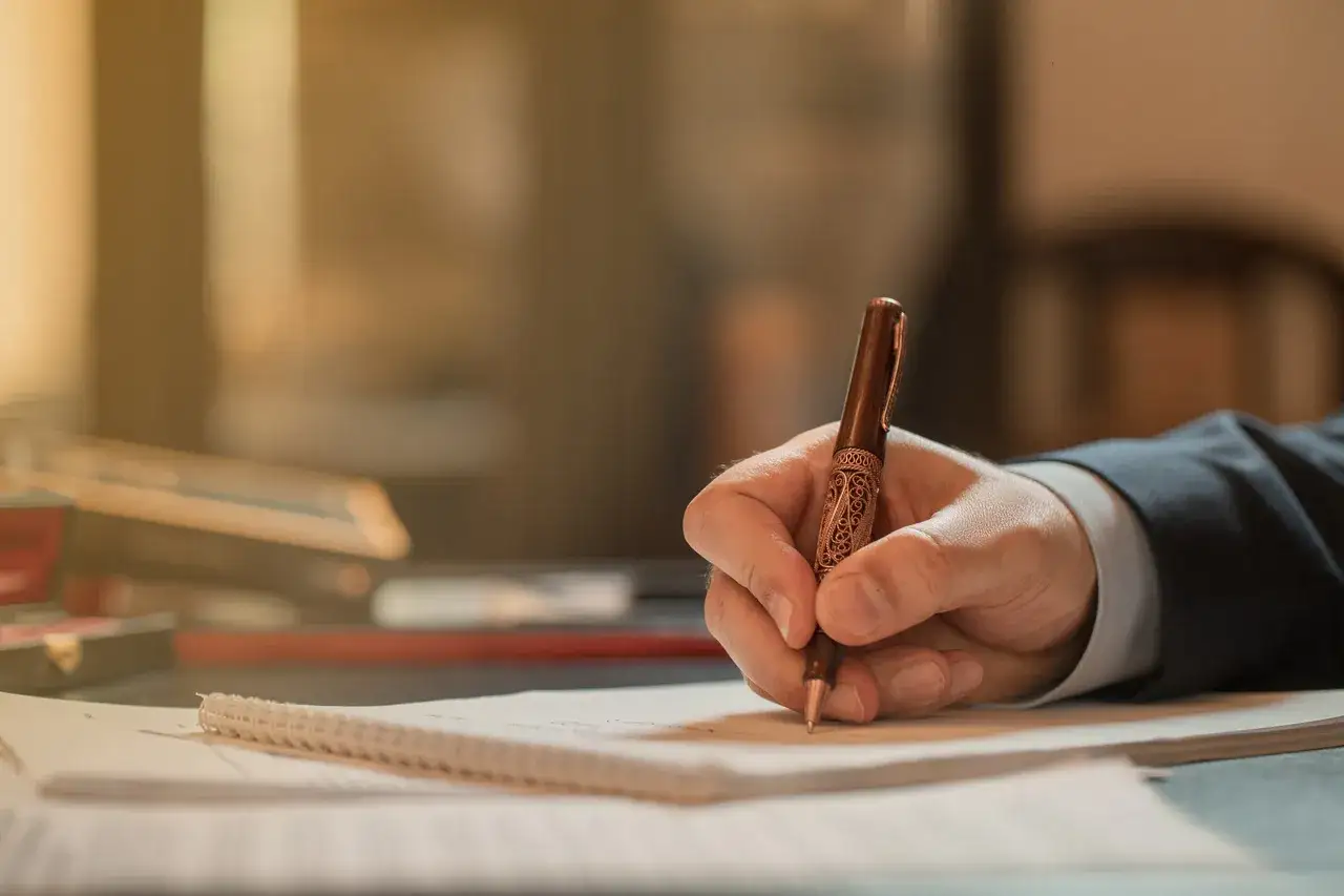 Dłoń pisze piórem po papierze, finalizując stwierdzenie nabycia spadku u notariusza.