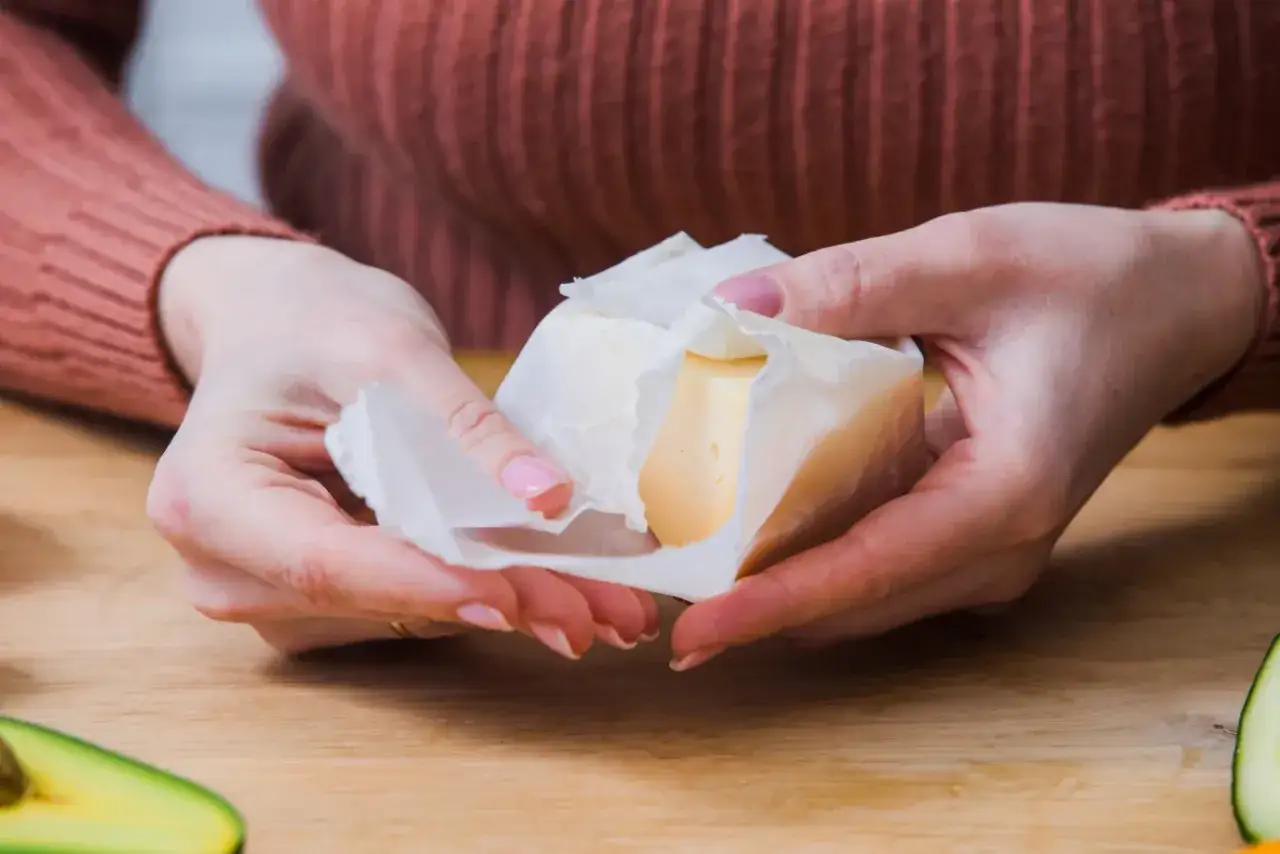 Dłonie rozwijają kostkę masła z papieru.
