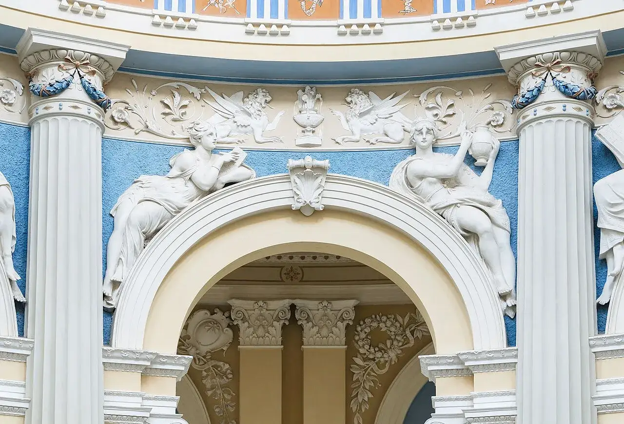 Barokowe stiuki: rzeźby kobiet, gryfy i ornamenty na tle błękitnej ściany.