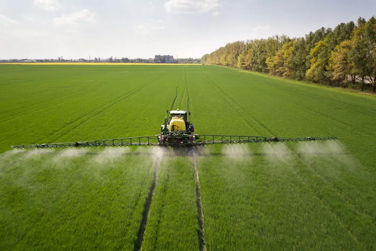 Traktor opryskuje zielone pole, rozpylając płyn. To nie jest adblue na trawnik, lecz środek ochrony roślin.