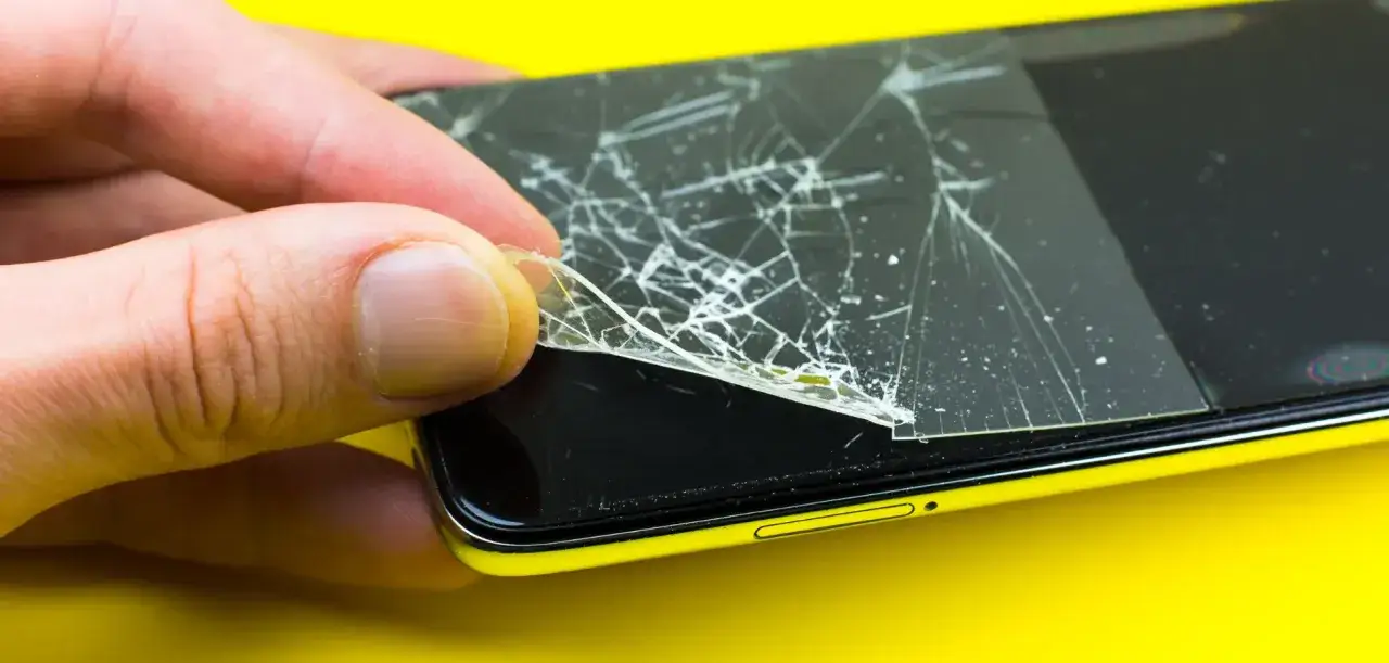 Dłoń zdejmuje pęknięte szkło hartowane 9h z ekranu telefonu.