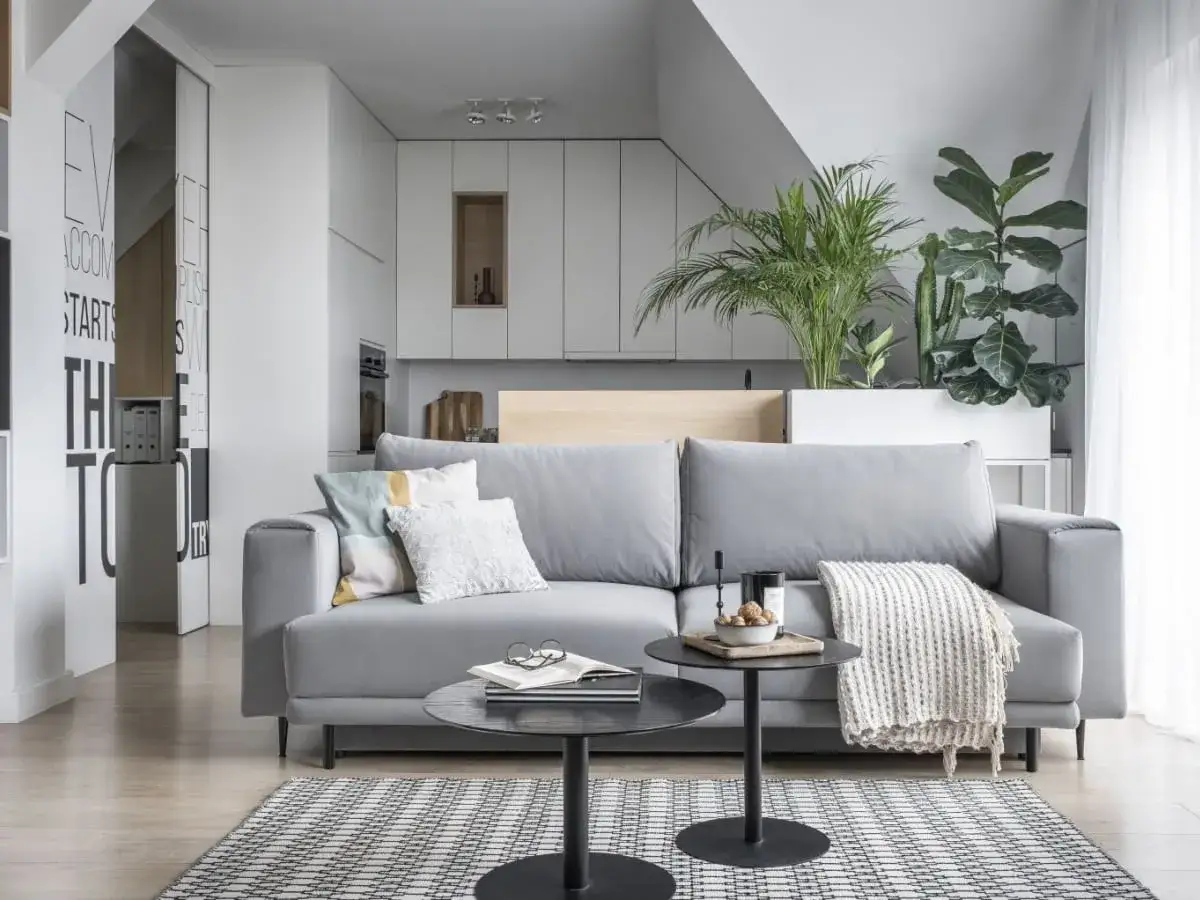 Nowoczesny salon z szarą kanapą i roślinami. Dowiedz się, jak zmienić wystrój pokoju tanim kosztem, dodając tekstylia i zieleń.