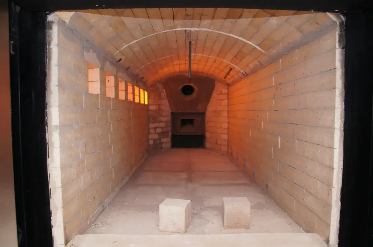 Wnętrze krematorium z ceglanymi ścianami i łukowym sufitem, oświetlone pomarańczowym blaskiem.