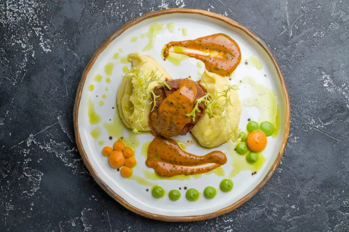 Talerz z pieczoną wieprzowiną, puree ziemniaczanym i sosami.
