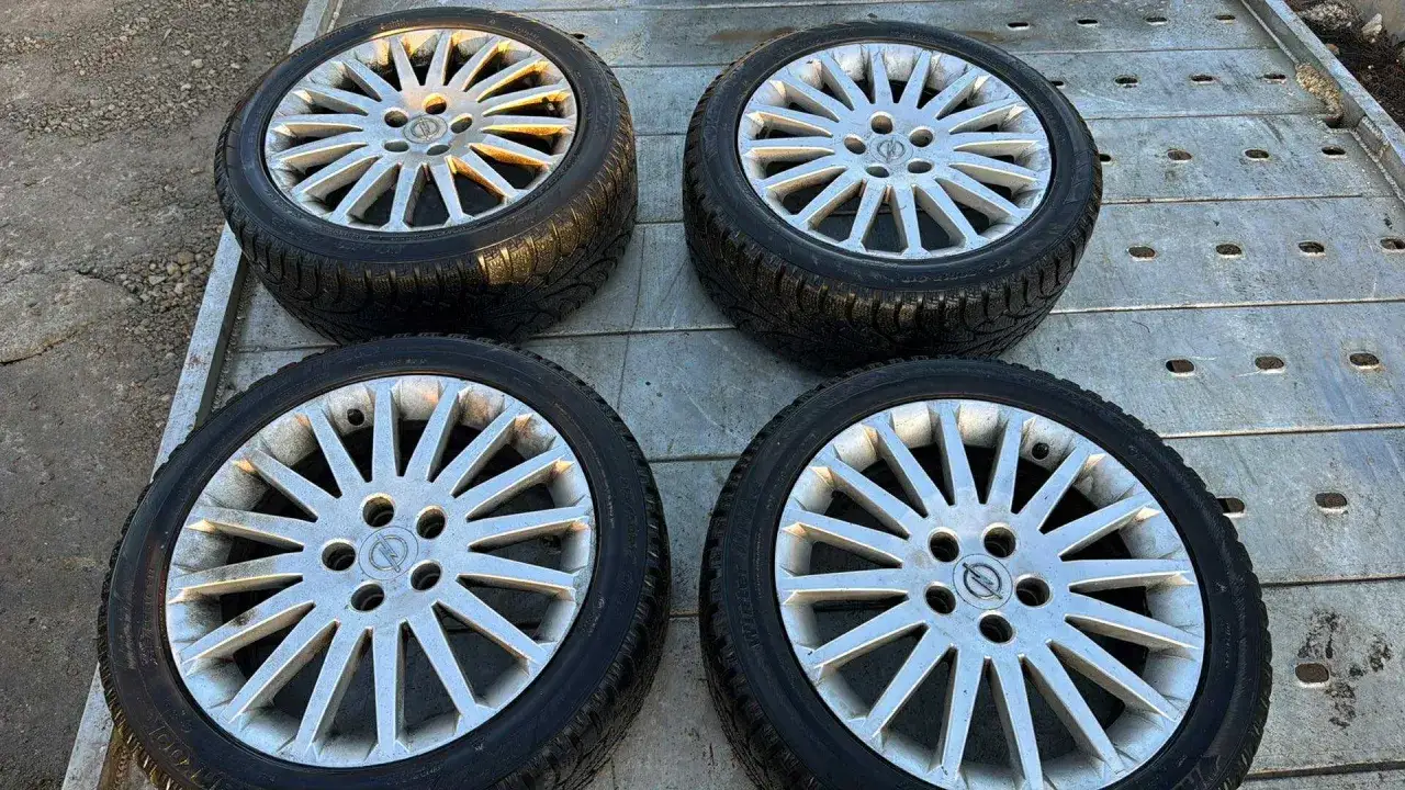 Cztery aluminiowe felgi z oponami zimowymi, z logo Opla, leżące na metalowej platformie.