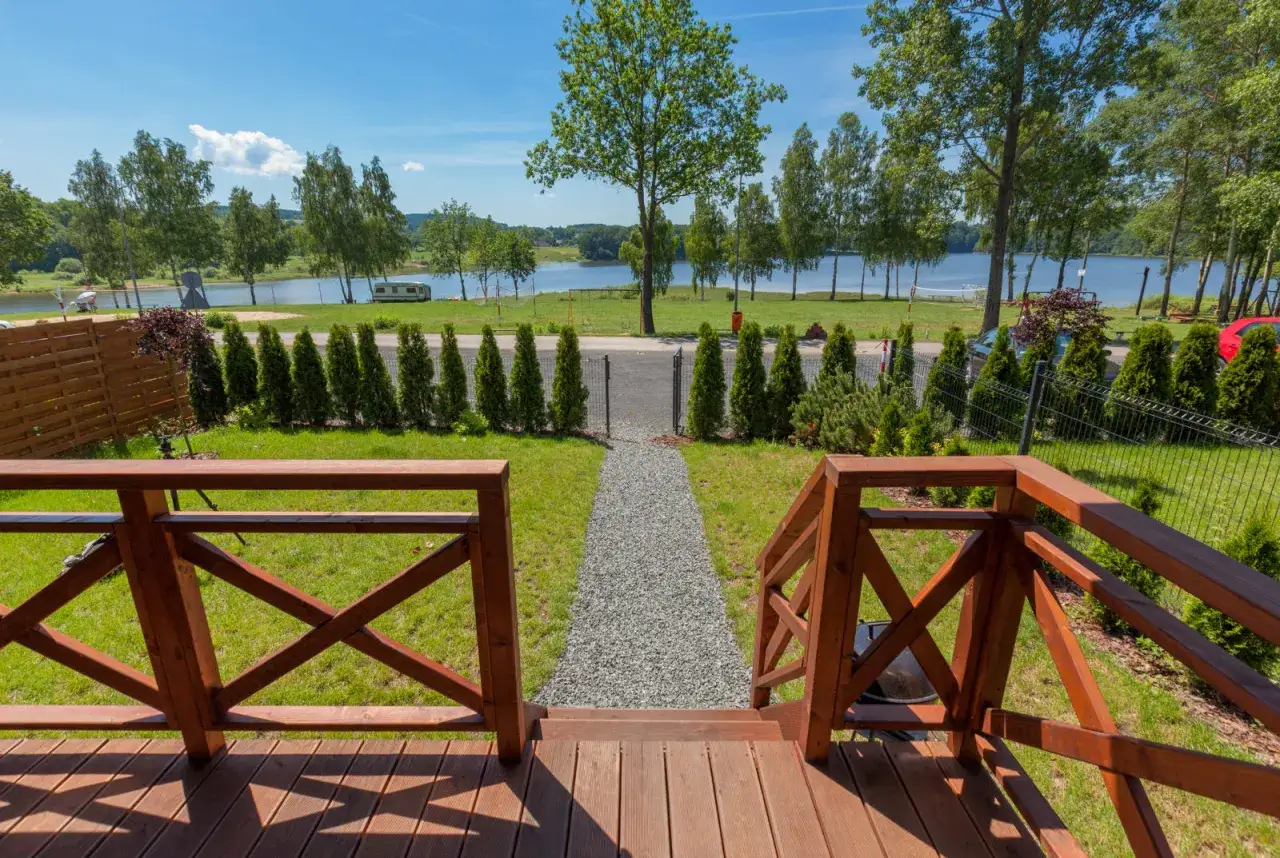 Drewniany taras z widokiem na jezioro, drzewa i zielony trawnik.