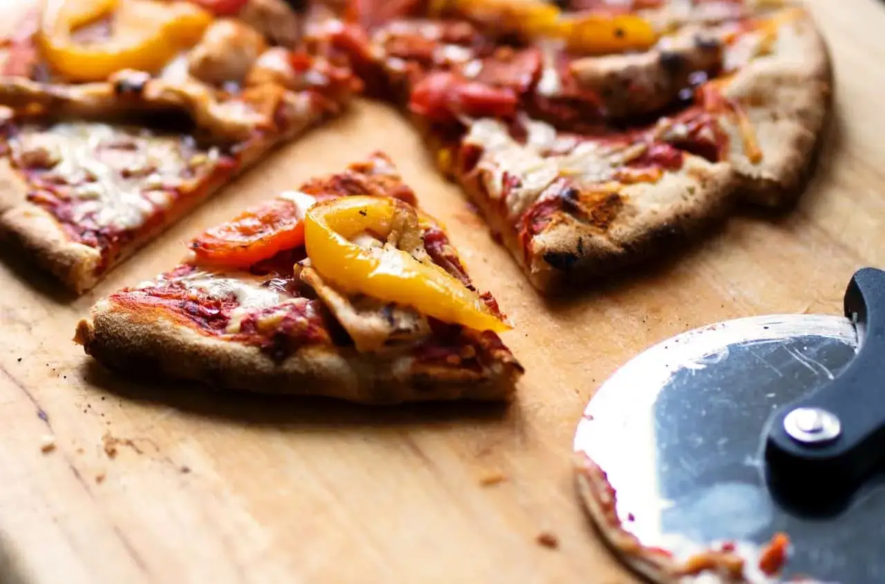 Kawałki pizzy z papryką i serem. Idealne, gdy zastanawiasz się, co można dać na pizzę. Obok leży nóż do pizzy.