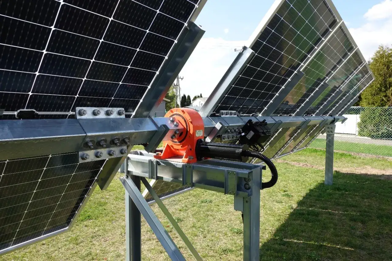 Mechanizm tracker pv z pomarańczową przekładnią i siłownikiem, obracający panele słoneczne na metalowej konstrukcji.