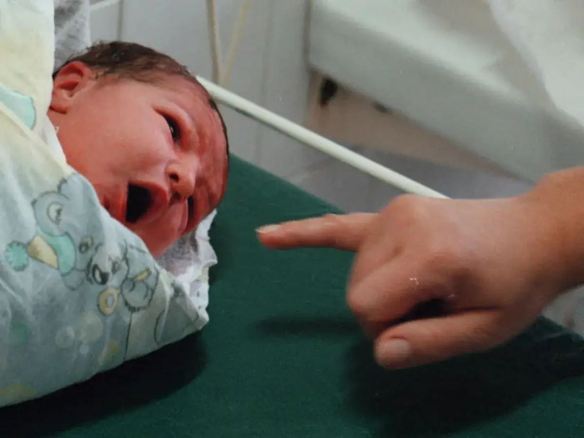 Noworodek w otulaczu z misiami, na którego palcem wskazuje dorosła dłoń.