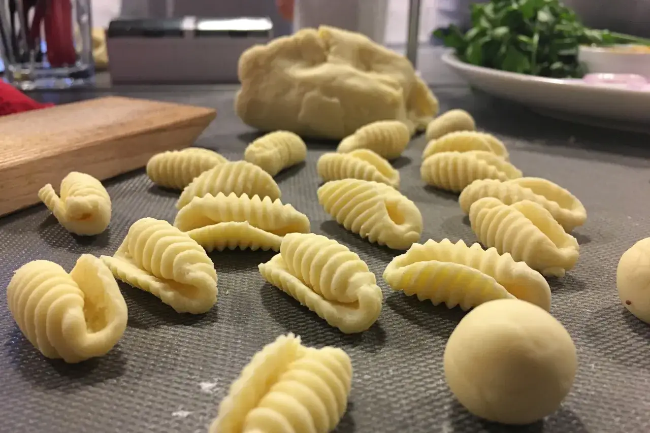 Świeży, domowy makaron w kształcie muszelek i innych form, leżący na szarej powierzchni.