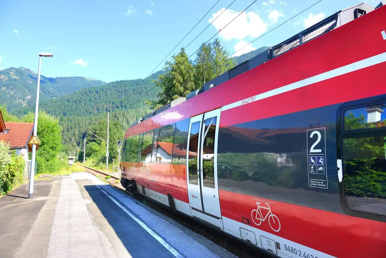 Czerwony pociąg na tle górskich krajobrazów. Chcesz wiedzieć, jak kupić bilet na pociąg w Niemczech? To proste, wystarczy podejść do kasy lub automatu.