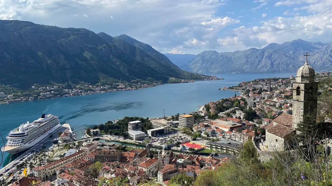 Widok na Zatokę Kotorską, z górami w tle, statkiem wycieczkowym i miastem. Czarnogóra ceny mogą być zaskakująco przystępne.