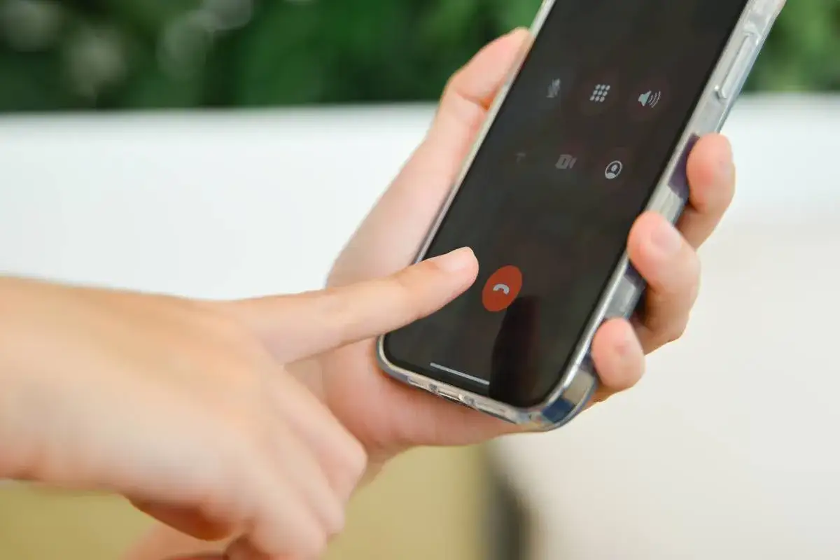 Dłoń naciska czerwony przycisk zakończenia rozmowy na ekranie smartfona, przypominając o kultowych dzwonkach na telefon.