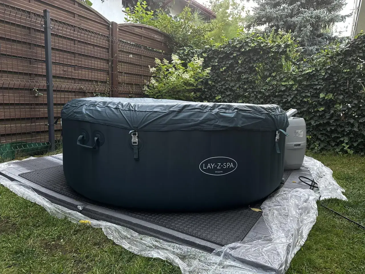 Nadmuchiwane jacuzzi Lay-Z-Spa Miami w ogrodzie, przykryte ciemnozieloną plandeką.
