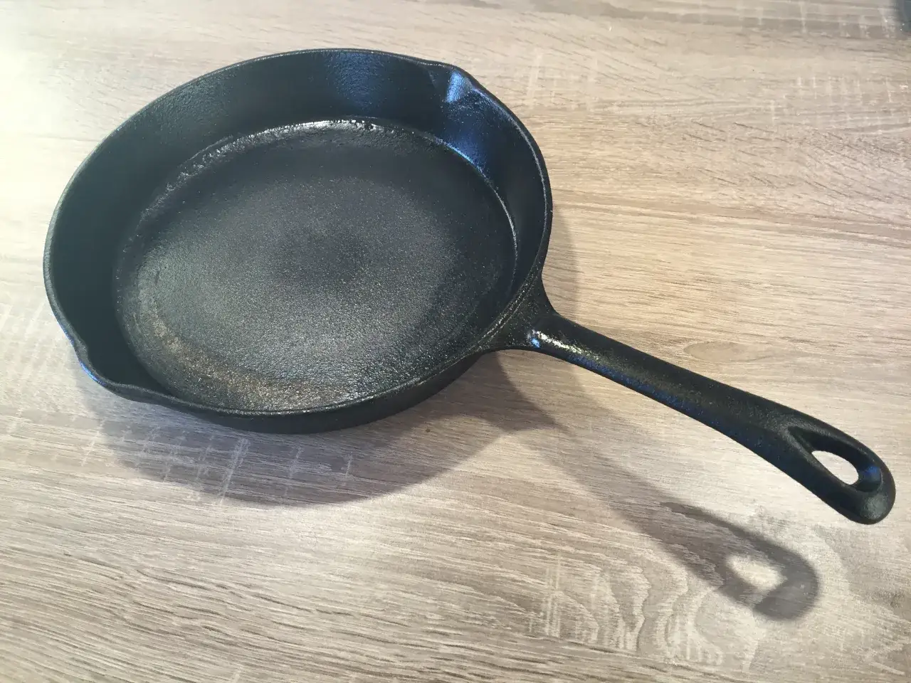 Czarna, żeliwna patelnia na drewnianym blacie. Dowiedz się, jak przygotować patelnię żeliwną do pierwszego użycia i jak o nią dbać.