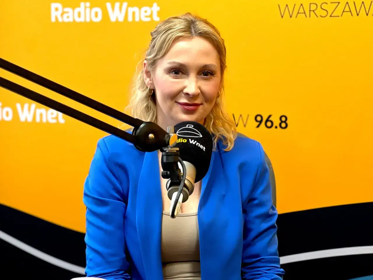 Joanna Miziołek, w wieku około 40 lat, w niebieskiej marynarce, udziela wywiadu w Radiu Wnet.