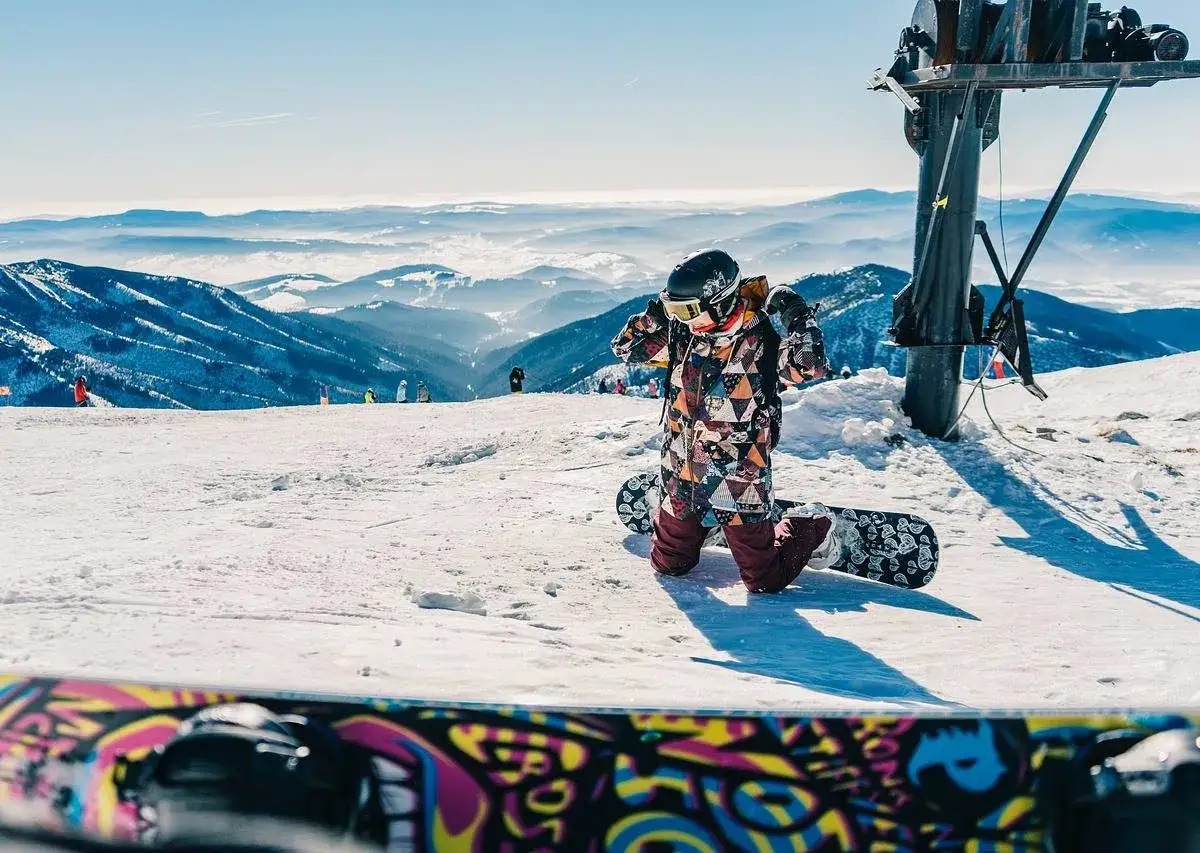 Dziecko w kolorowym kombinezonie przygotowuje się do zjazdu na snowboardzie. Idealne miejsce, gdzie na narty w Czechach z dziećmi.