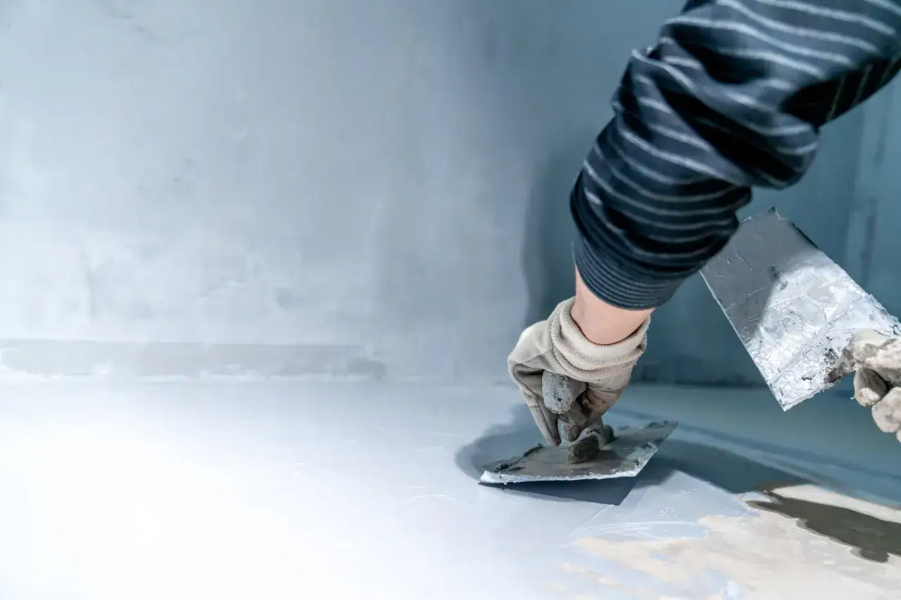 Ręce w rękawiczkach rozprowadzają gładź szpachlową po ścianie. Trudno ocenić, ile gipsu na m2 potrzeba, ale praca idzie sprawnie.