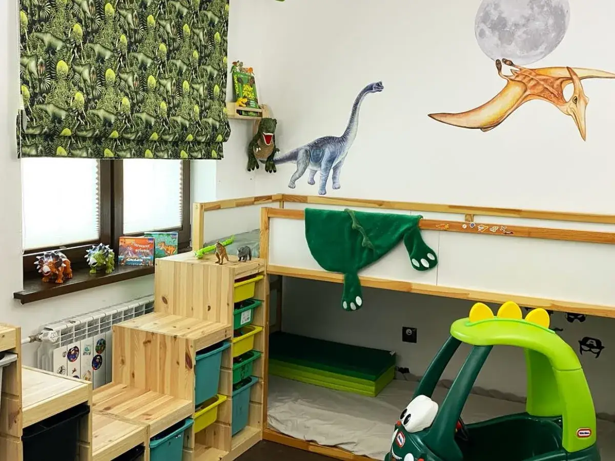 Pokój dla chłopca 7 lat inspiracje: dinozaury na ścianach, zasłonach i zabawkach. Drewniane schodki do łóżka piętrowego i zielony samochodzik.