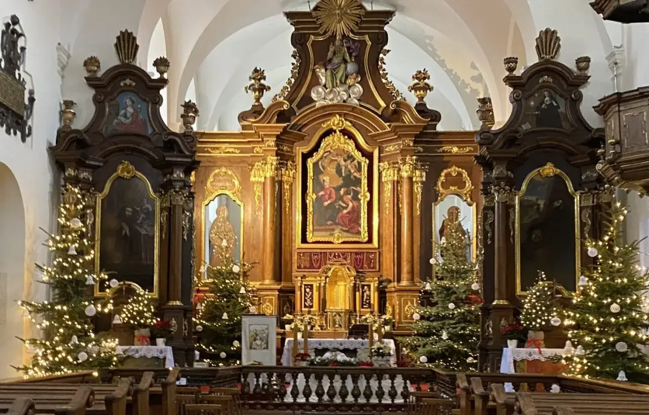 Ołtarz główny kościoła z obrazem Matki Boskiej, ozdobiony choinkami i iluminacjami.