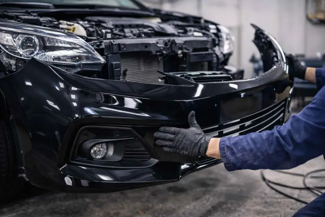 Mechanik w czarnej rękawiczce przykłada dłoń do czarnego zderzaka samochodu.