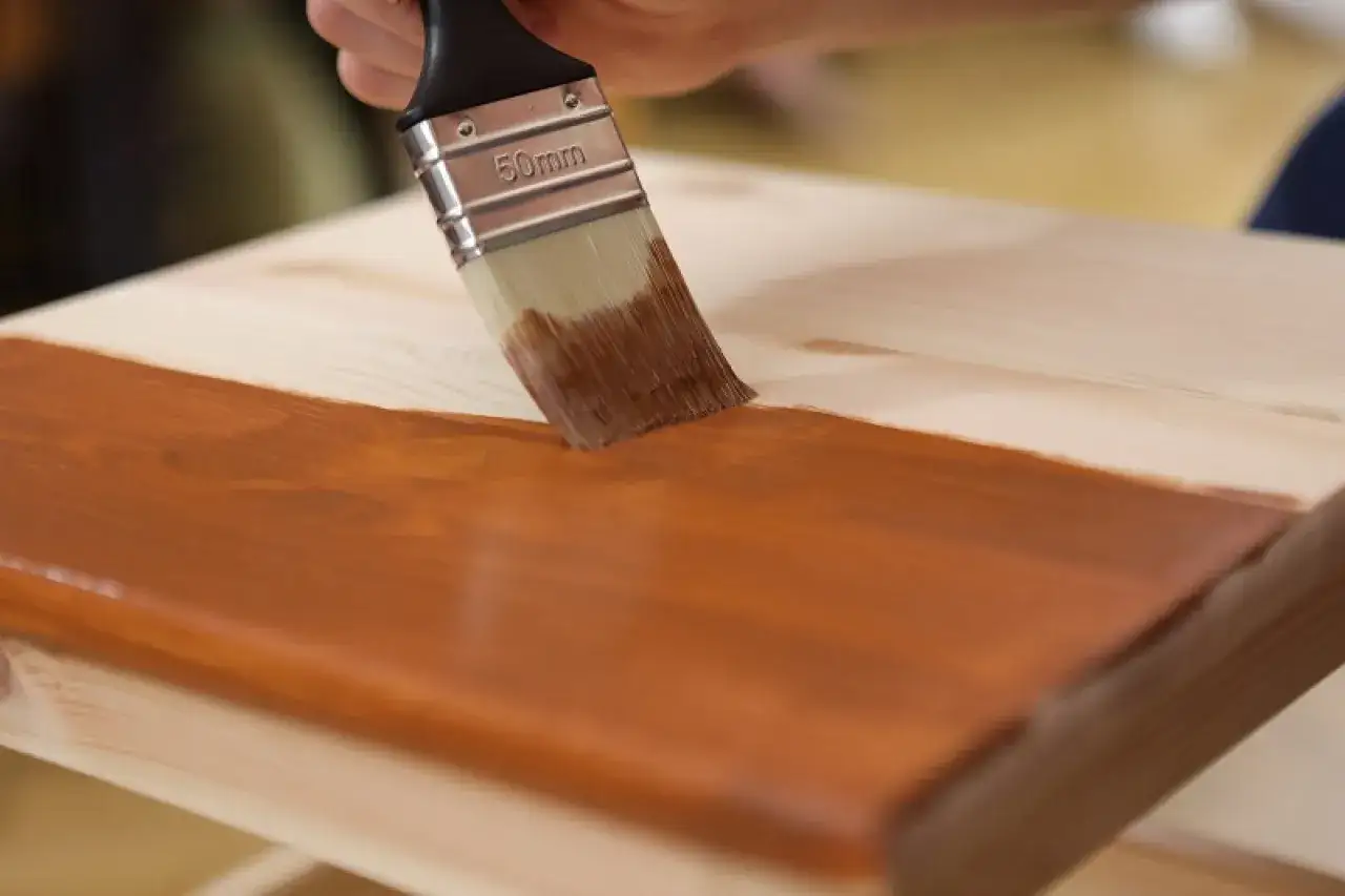 Pędzel nakłada brązowy impregnat na drewno, chroniąc je przed pękaniem i nadając mu nowy wygląd.