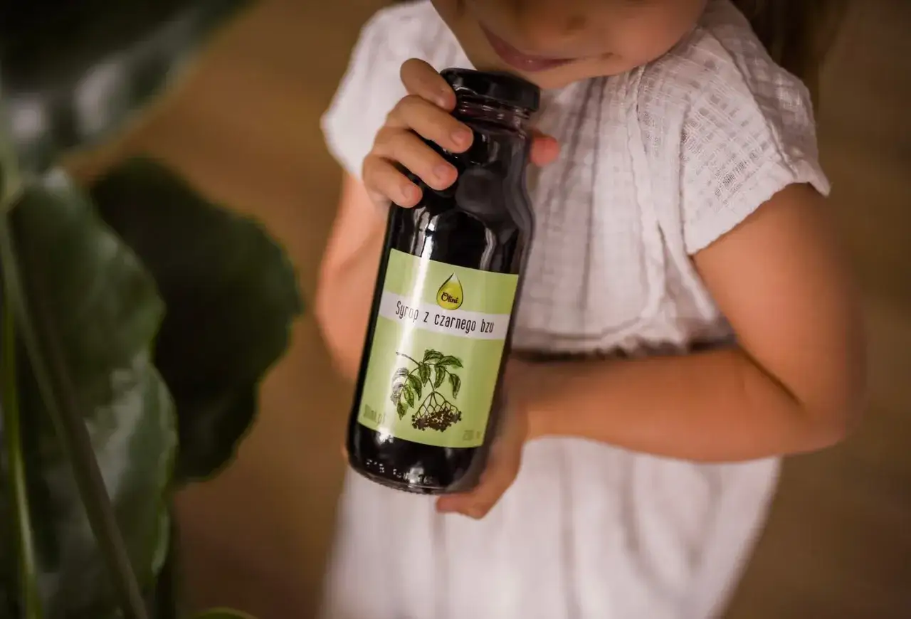 Dziecko trzyma butelkę syropu z czarnego bzu, który jest naturalnym wsparciem dla odporności.