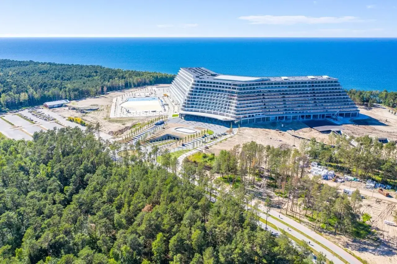 Nowoczesny hotel z basenem i widokiem na morze, otoczony lasem.