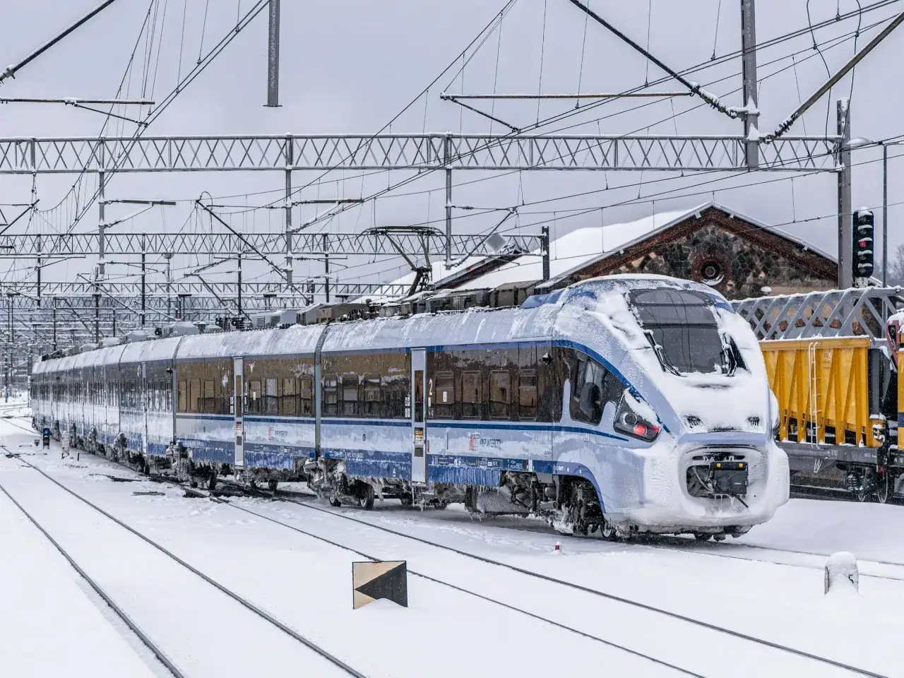Pociąg PKP Intercity pokryty śniegiem na tle zimowego krajobrazu.