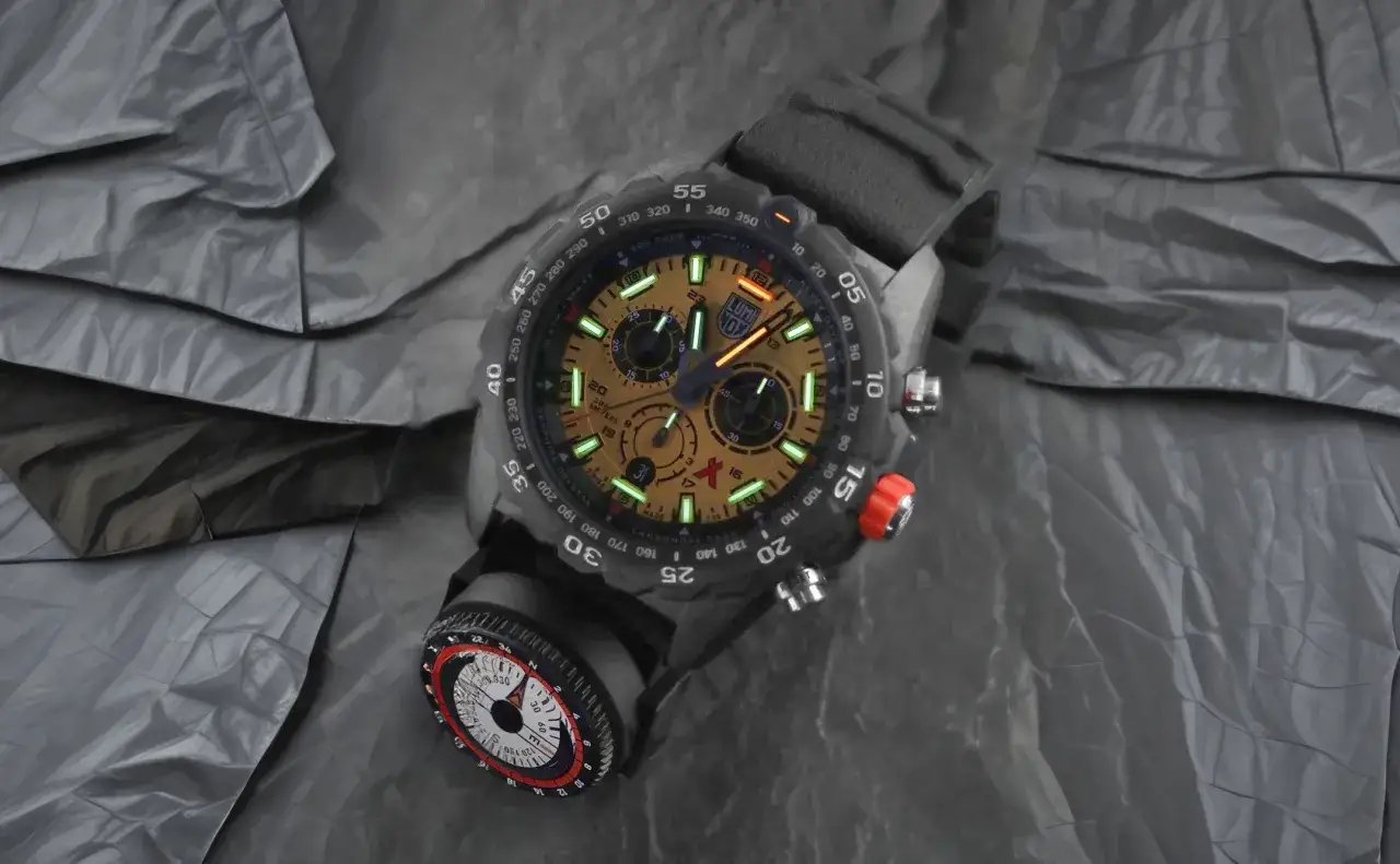 Męski zegarek z tarczą i kompasem, na tle pogniecionej tkaniny.