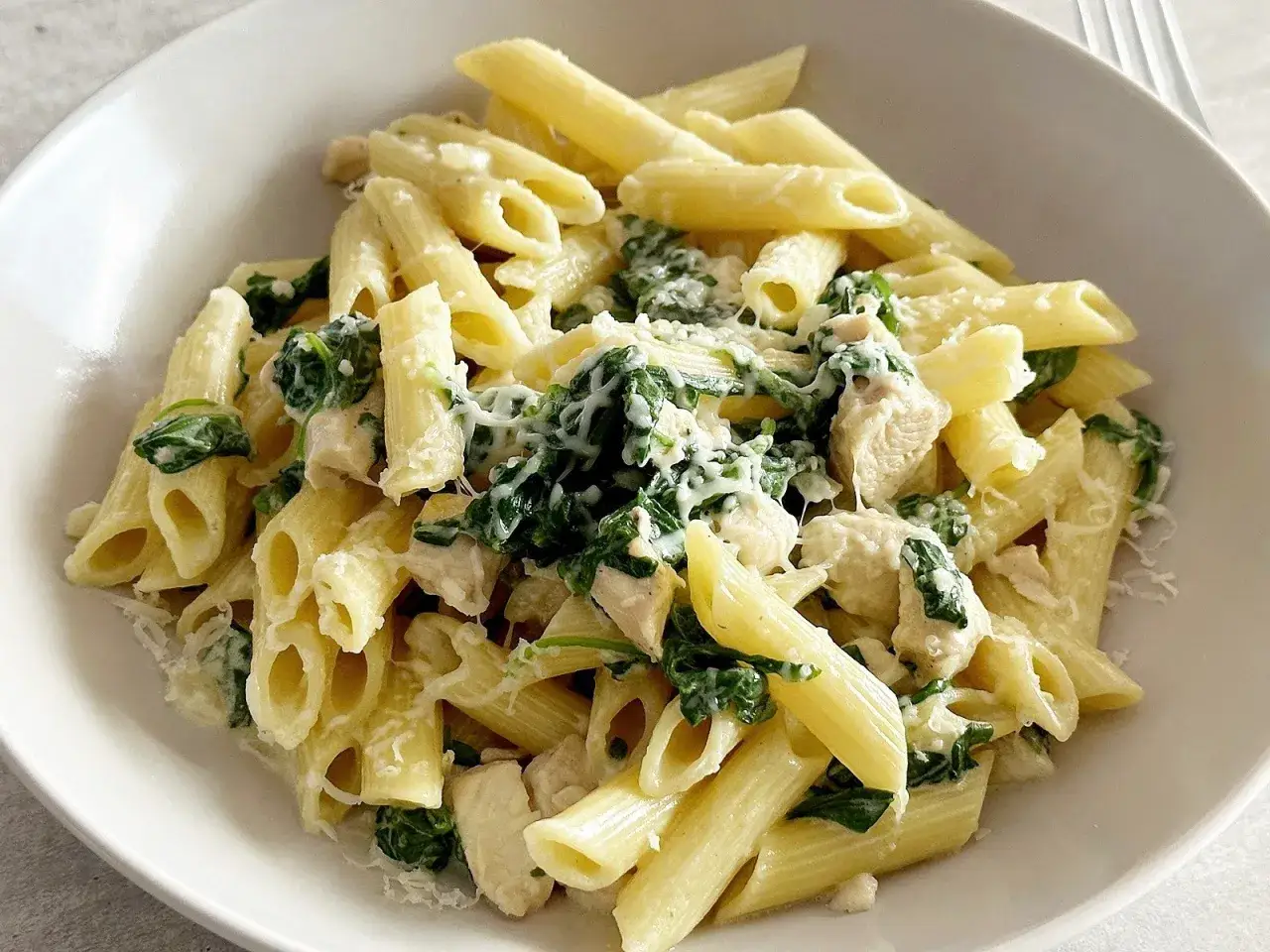 Penne z kurczakiem, szpinakiem i fetą, posypane parmezanem. Pyszne danie, które zachwyci każdego.